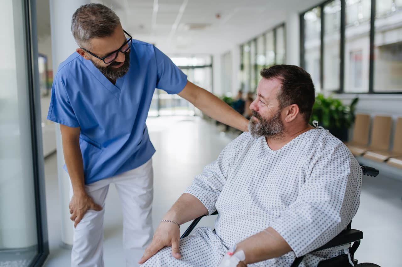 Close up of supportive doctor talking with worried overweight patient in wheelchair. Illnesses and diseases in middle aged men's health. Compassionate physician supporting stressed patient. Concept of health risks of overwight and obesity.