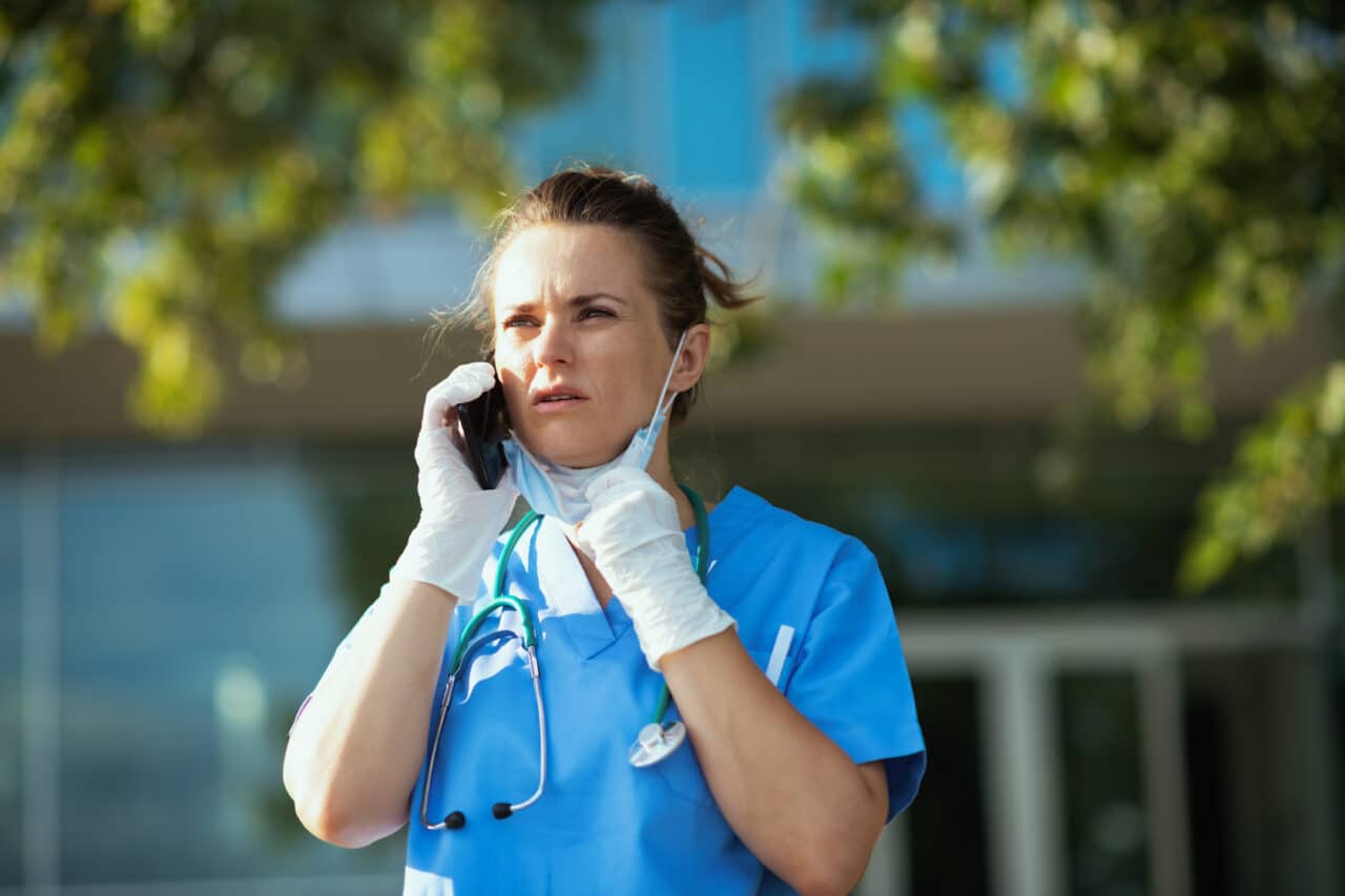 unhappy modern physician woman using phone outdoors near clinic