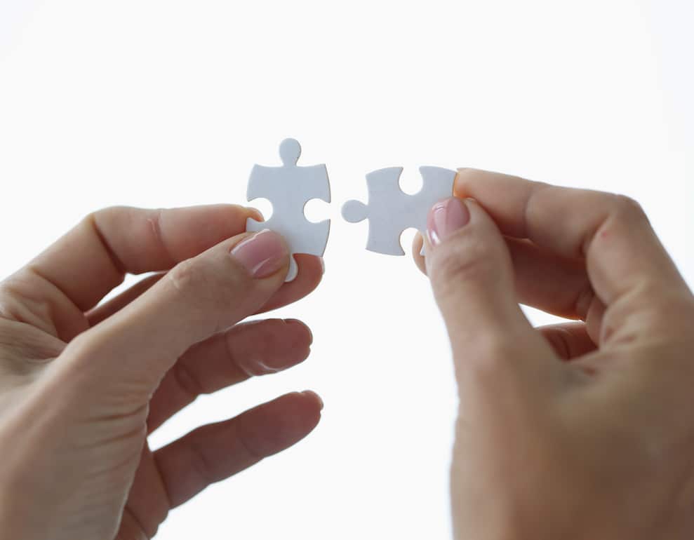 Female hands holding two white puzzle pieces closeup