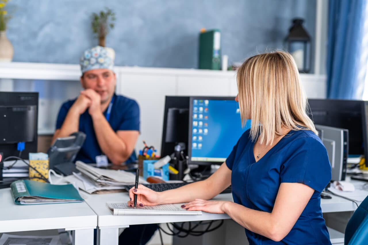 Two doctors discussing medical expertise in office at computer. Man and woman medics.